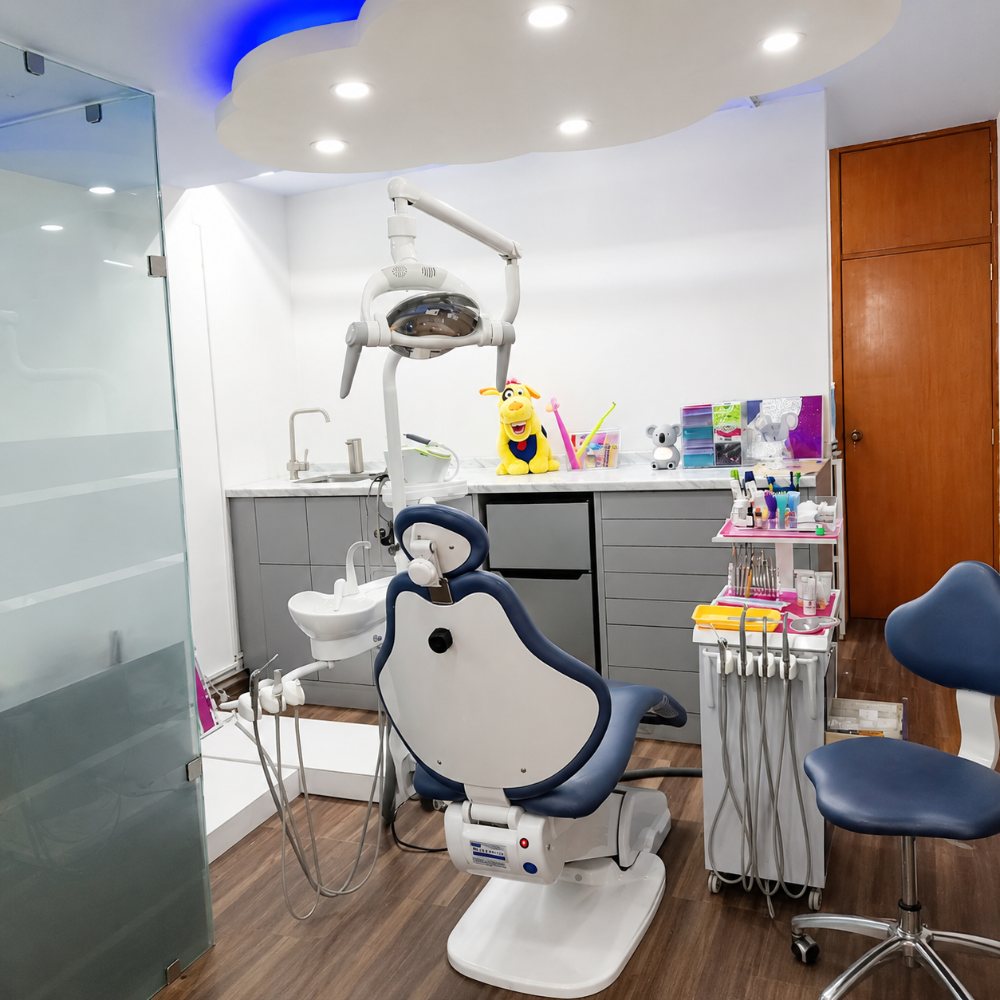Área clínica con sillón dental azul, lámpara y unidad de trabajo